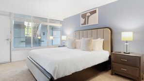 A bedroom with a large bed, a nightstand, a lamp, a window with blinds, and a wall-mounted artwork. - Landing | Amazing 1BD, Clubhouse, Gym (Kissimmee)