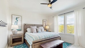 A bedroom with a wooden bed, two bedside tables with lamps, a ceiling fan, and a view of trees through the window. - New dog-friendly home with a private pool near the Gulf (Gulf Shores)