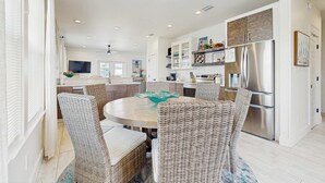 A modern kitchen with a central island, stainless steel appliances, and wicker chairs around a round table. - New dog-friendly home with a private pool near the Gulf (Gulf Shores)