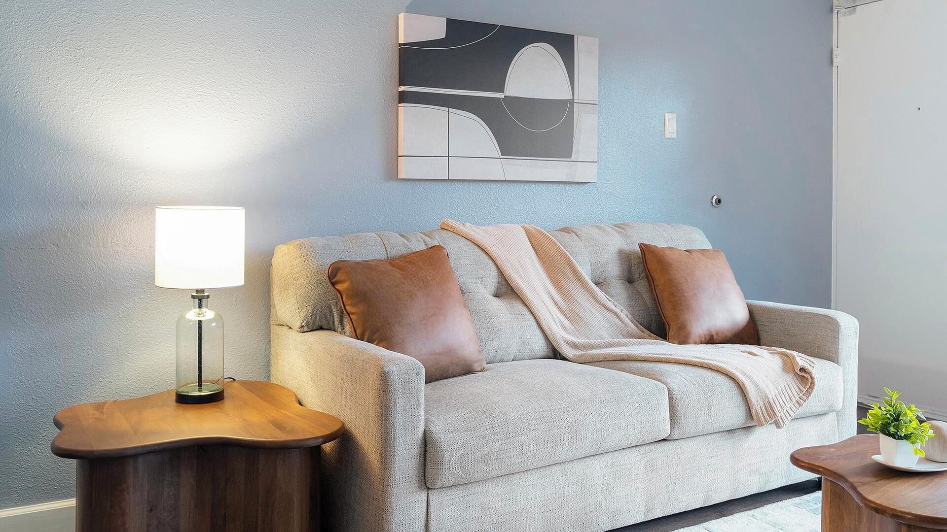 A living room with a sofa, two side tables, a lamp, and a wall art piece.