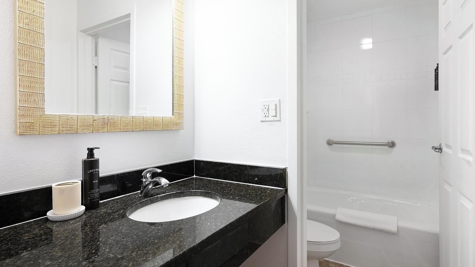 Une salle de bain avec un lavabo en marbre noir, des toilettes blanches et un espace douche.