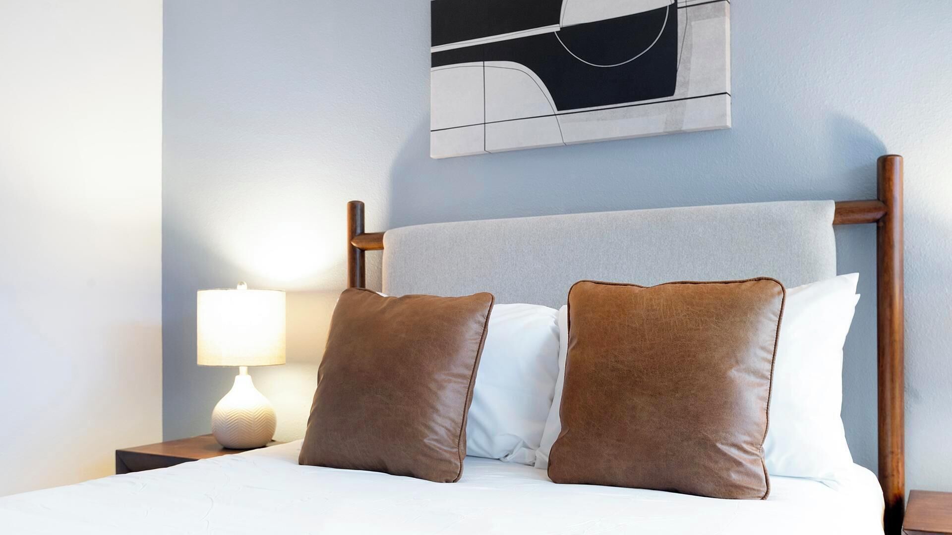 Uma cama com duas almofadas, um abajur e uma obra de arte abstrata na parede.