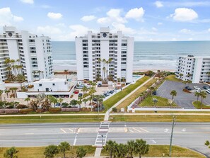 A coastal hotel with multiple white buildings, a parking area, and a view of the ocean. - Oceanwalk 13-305 (New Smyrna Beach)