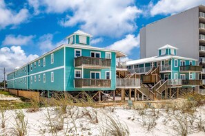 Een hotel aan het strand met meerdere verdiepingen, houten balkons en een zandstrand op de voorgrond.