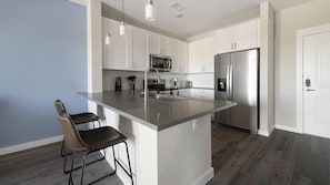 Una cocina moderna con una isla central, electrodomésticos de acero inoxidable y un taburete de bar.