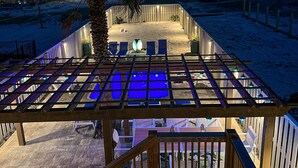 Ein Poolbereich mit einer Holz-Pergola, Liegestühlen und einem Sandstrand.