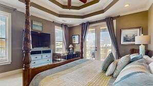 Ein Schlafzimmer mit Himmelbett, Schreibtisch, Fernseher und einem Balkon mit Vorhängen.