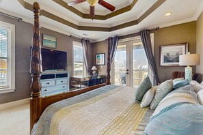 Ein Schlafzimmer mit Himmelbett, Schreibtisch, Fernseher und einem Balkon mit Vorhängen.