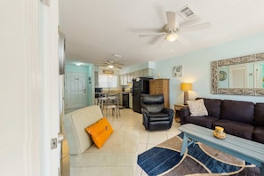 A living room with a sofa, armchair, coffee table, and a dining area with a table and chairs. - Home w/partial ocean views, internet, washer/dryer, central AC (Gulf Shores)