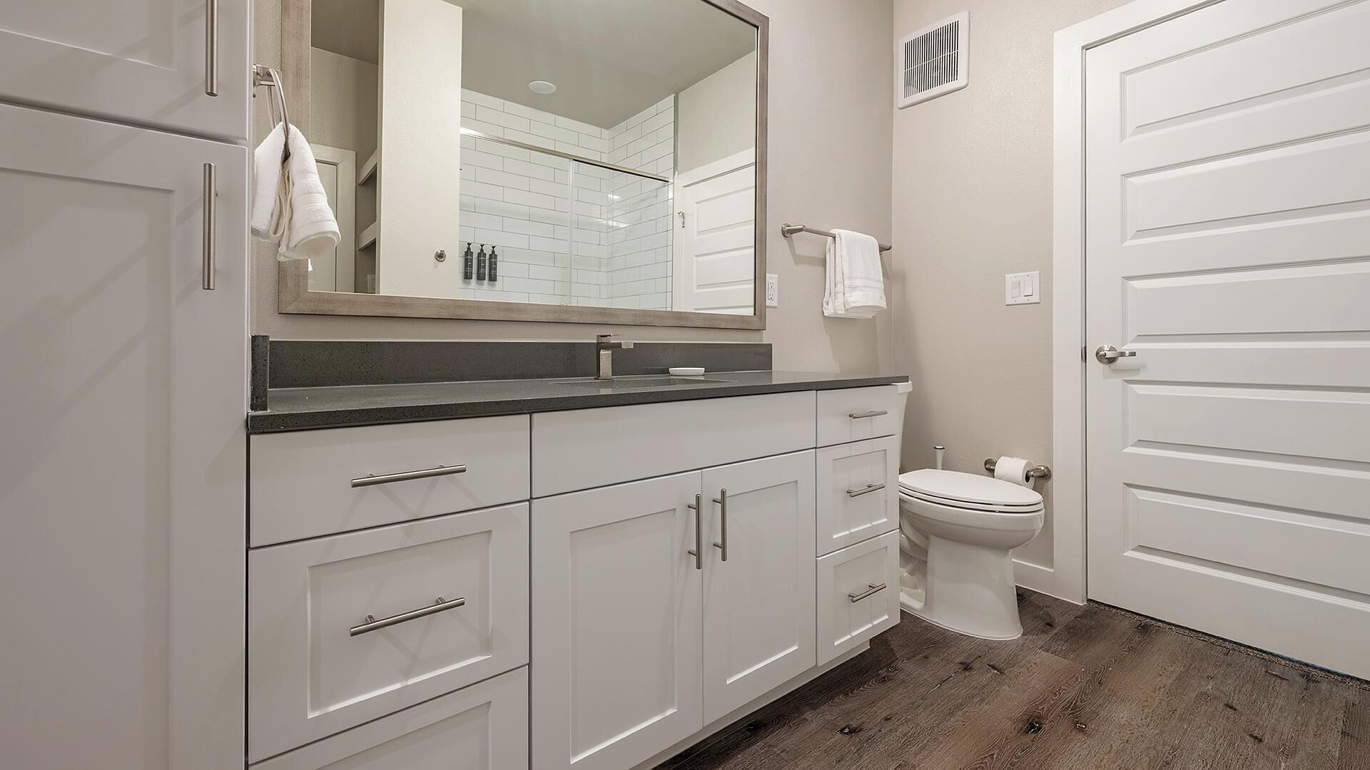 Un baño moderno con muebles blancos, un espejo grande, un inodoro y una zona de ducha.