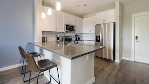 Una cocina moderna con gabinetes blancos, electrodomésticos de acero inoxidable, una isla grande con taburetes y luminarias colgantes.