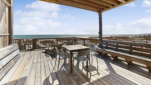 Une terrasse en bois avec une table et des chaises, donnant sur une plage.