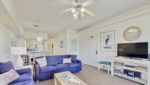 Un salon avec un canapé bleu, une table basse en bois, un téléviseur et un ventilateur de plafond.