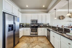 A kitchen with white cabinets, stainless steel appliances, a granite countertop, and a tiled floor. - Luxurious Gulf-front home w direct beach access, close to shops & dining (Gulf Shores)
