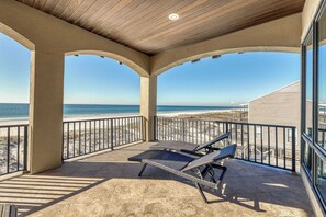 A covered outdoor area with a view of the beach, featuring a lounge chair and a table. - Luxurious Gulf-front home w direct beach access, close to shops & dining (Gulf Shores)
