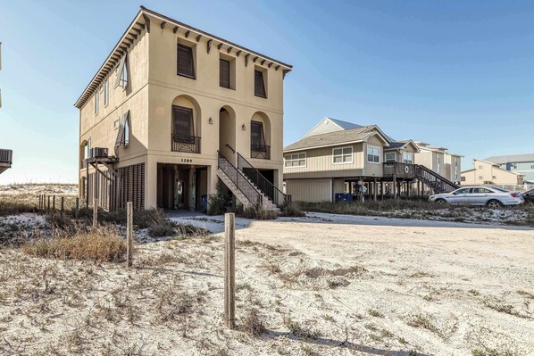 A two-story building with a beige facade, a staircase leading to the entrance, and a clear sky. - Luxurious Gulf-front home w direct beach access, close to shops & dining (Gulf Shores)