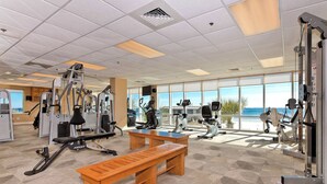 Ein Fitnessraum mit Trainingsgeräten, einer hölzernen Bank und großen Fenstern mit Blick.