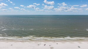 Ein Strand mit Wellen, blauem Himmel und einigen Personen.