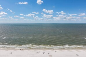 Ein Strand mit Wellen, blauem Himmel und einigen Personen.