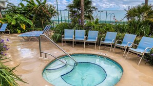 Piscina com placa indicando profundidade de 0,9 metros, rodeada por espreguiçadeiras e plantas tropicais.