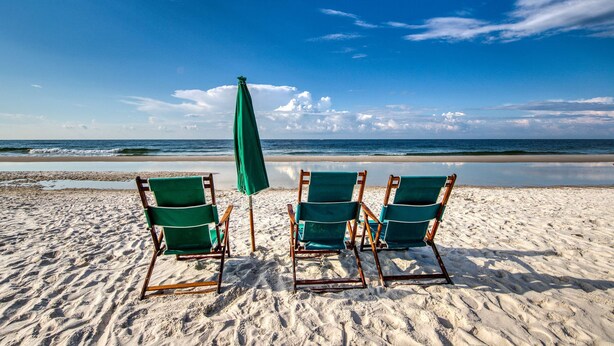 Uma praia com três espreguiçadeiras verdes e um guarda-sol verde.