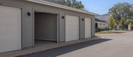A row of closed garage doors with a clear driveway leading to a building.