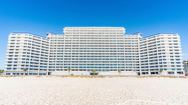 Un hotel grande de varios pisos con una fachada simétrica, situado en una playa arenosa.
