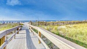 Pasarela de madera que lleva a una playa con cielo despejado.