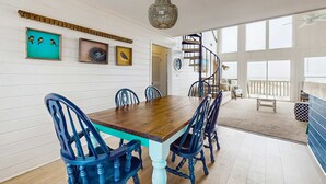 A dining area with a wooden table and blue chairs, white walls, and a chandelier. - Centrally-located Gulf front paradise wfurnished sun deck & gorgeous water view (Gulf Shores)
