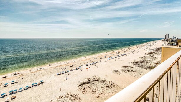 Ein Strand mit Sonnenschirmen und Menschen, ein klarer Himmel und Gebäude im Hintergrund.