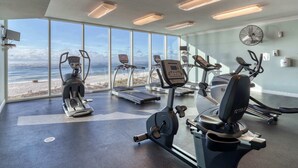 Ein Fitnessraum mit Cardiogeräten, Laufband und Blick auf den Strand.