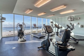 Ein Fitnessraum mit Cardiogeräten, Laufband und Blick auf den Strand.
