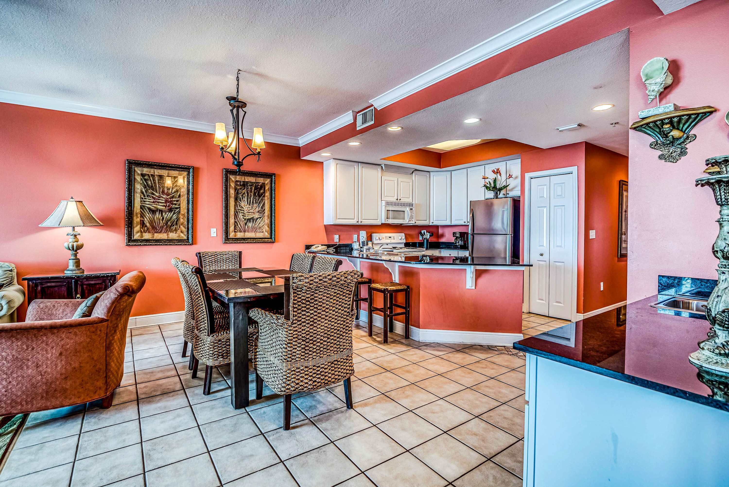 A dining area with a table and chairs, a kitchen with white cabinets, and a red accent wall.