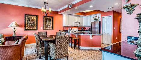 A dining area with a table and chairs, a kitchen with white cabinets, and a red accent wall.