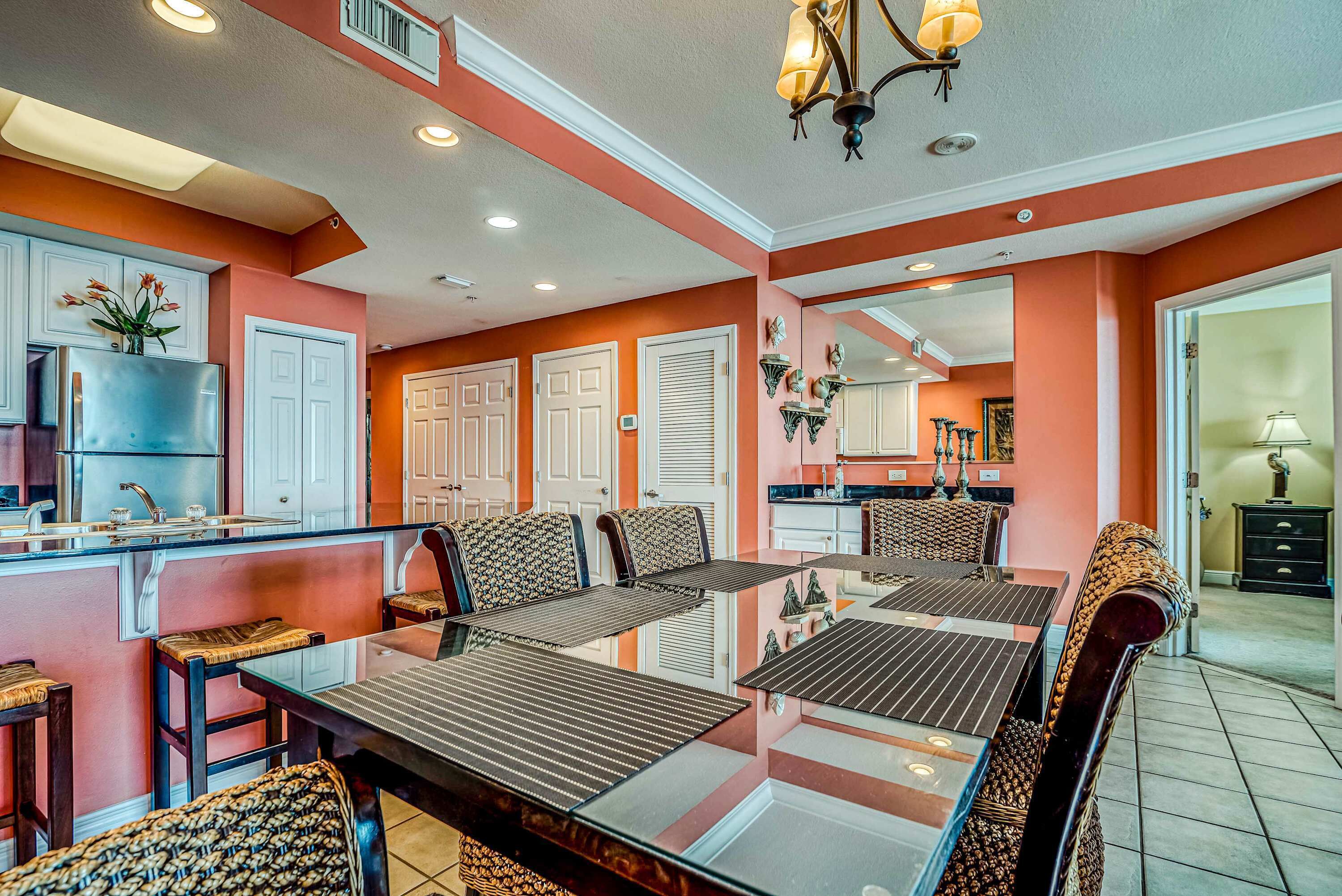 A spacious dining area with a glass-top table, multiple chairs, and a kitchen in the background.