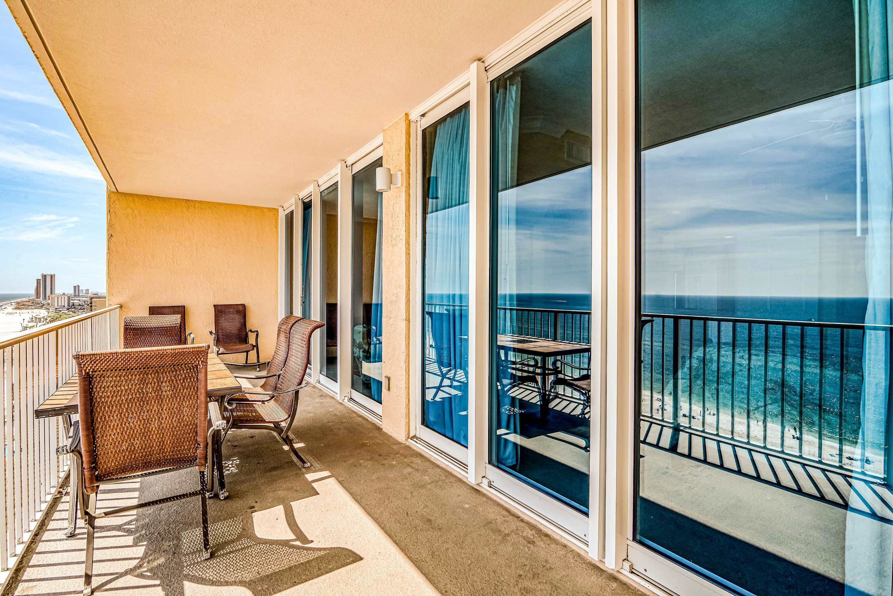 A balcony with a view of the ocean, wicker chairs, and a table.