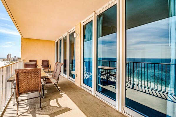 A balcony with a view of the ocean, wicker chairs, and a table. - Gulf front condo with multiple community pools, a private balcony, & gym (Gulf Shores)