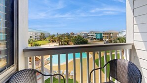En balkong med utsikt över en swimmingpool, solstolar och ett bostadsområde.