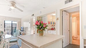Una habitación con kitchenette, un comedor con sillas, un ventilador de techo y una puerta que da a un baño.