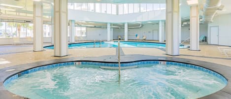 An indoor swimming pool with clear water, a hot tub, and lounge chairs.