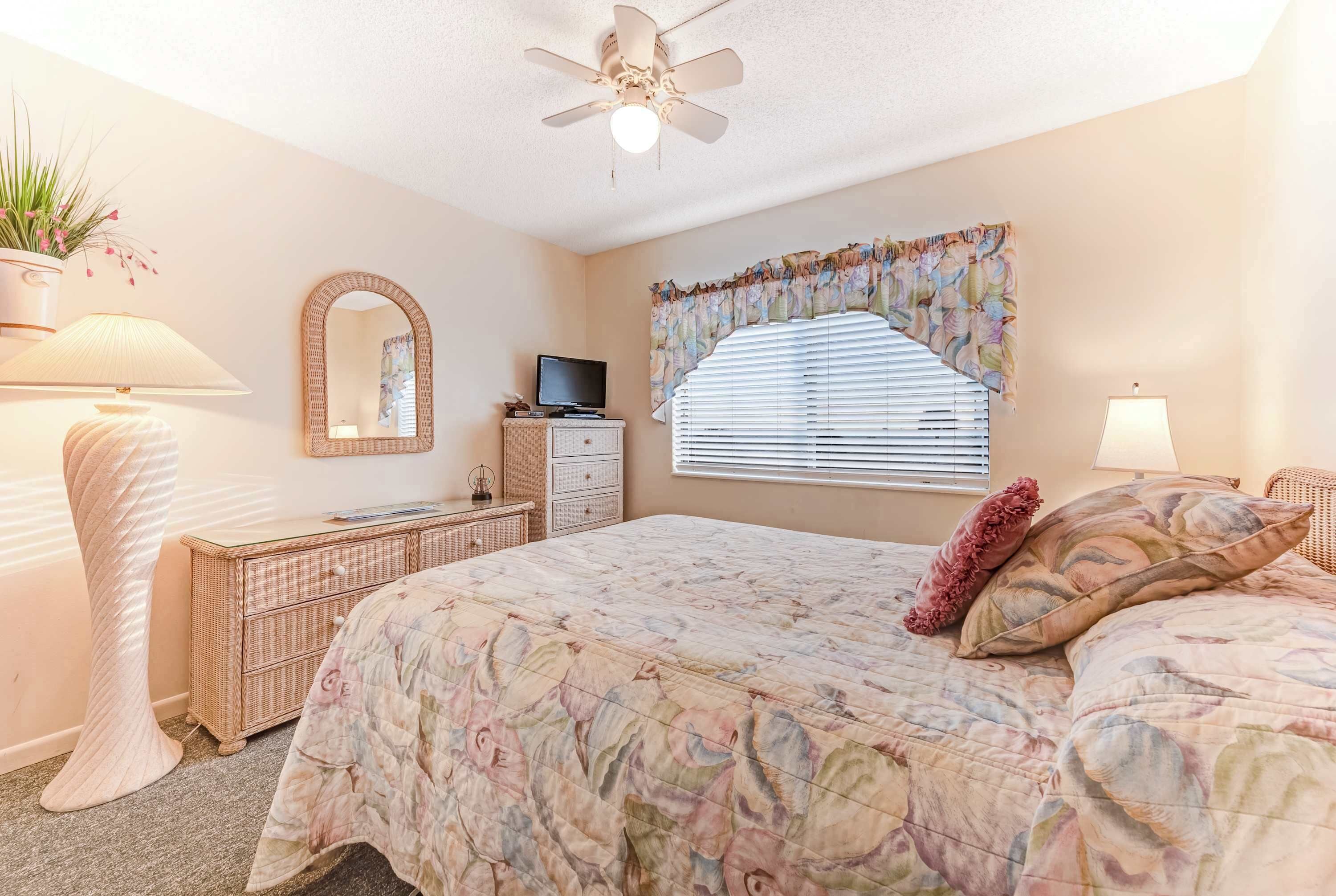 Une chambre à coucher comprenant un lit, une commode, un téléviseur et un ventilateur de plafond.
