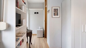 A narrow hallway with a white wardrobe, a small table with a kettle, and a television on a shelf. - Annex Bedroom – Oporto Garden (Porto)