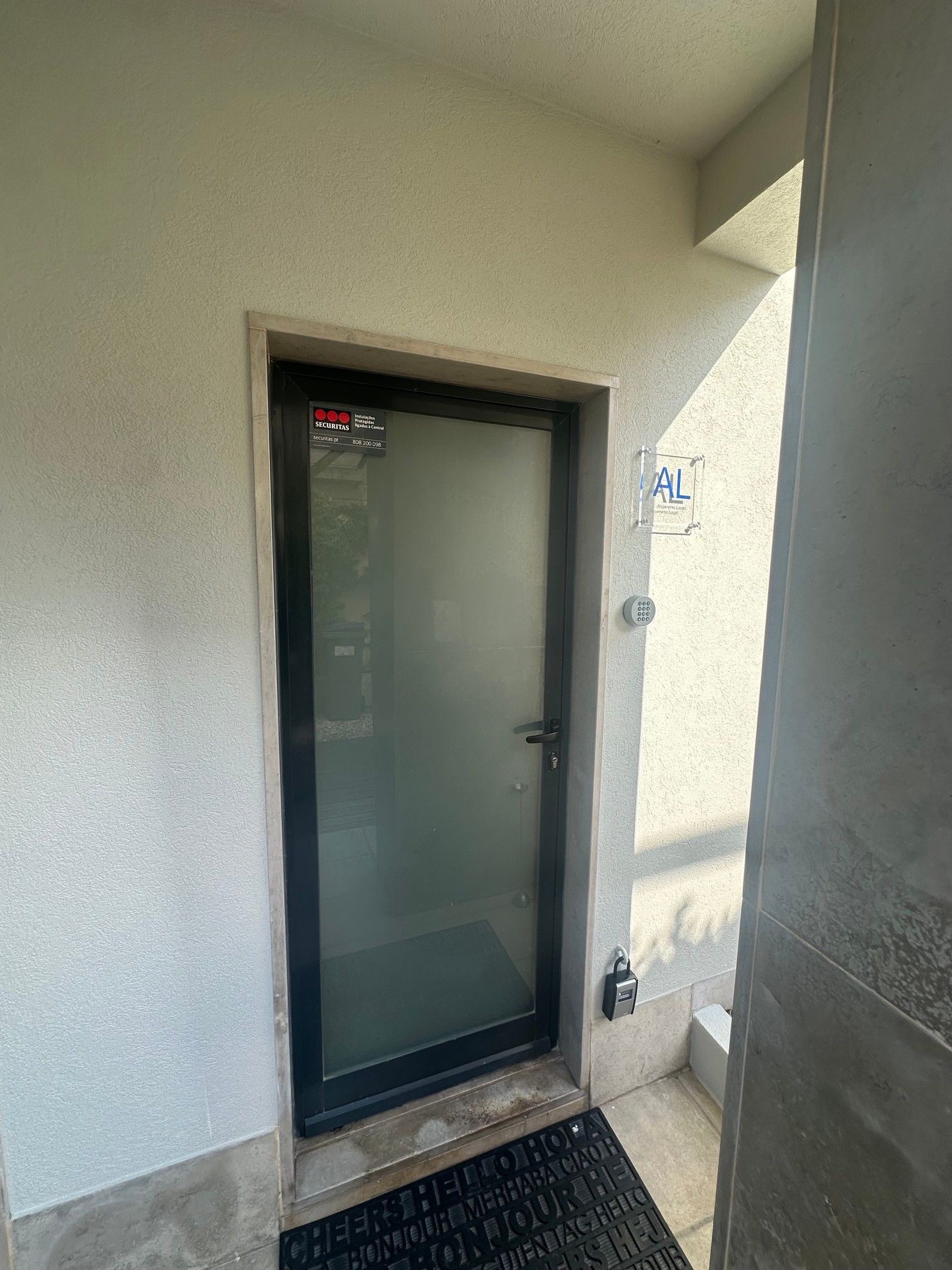 Une porte dotée d’une serrure de sécurité et d’un clavier, une petite marche menant à cette porte, et une plaque fixée au mur portant l’inscription « AL ».