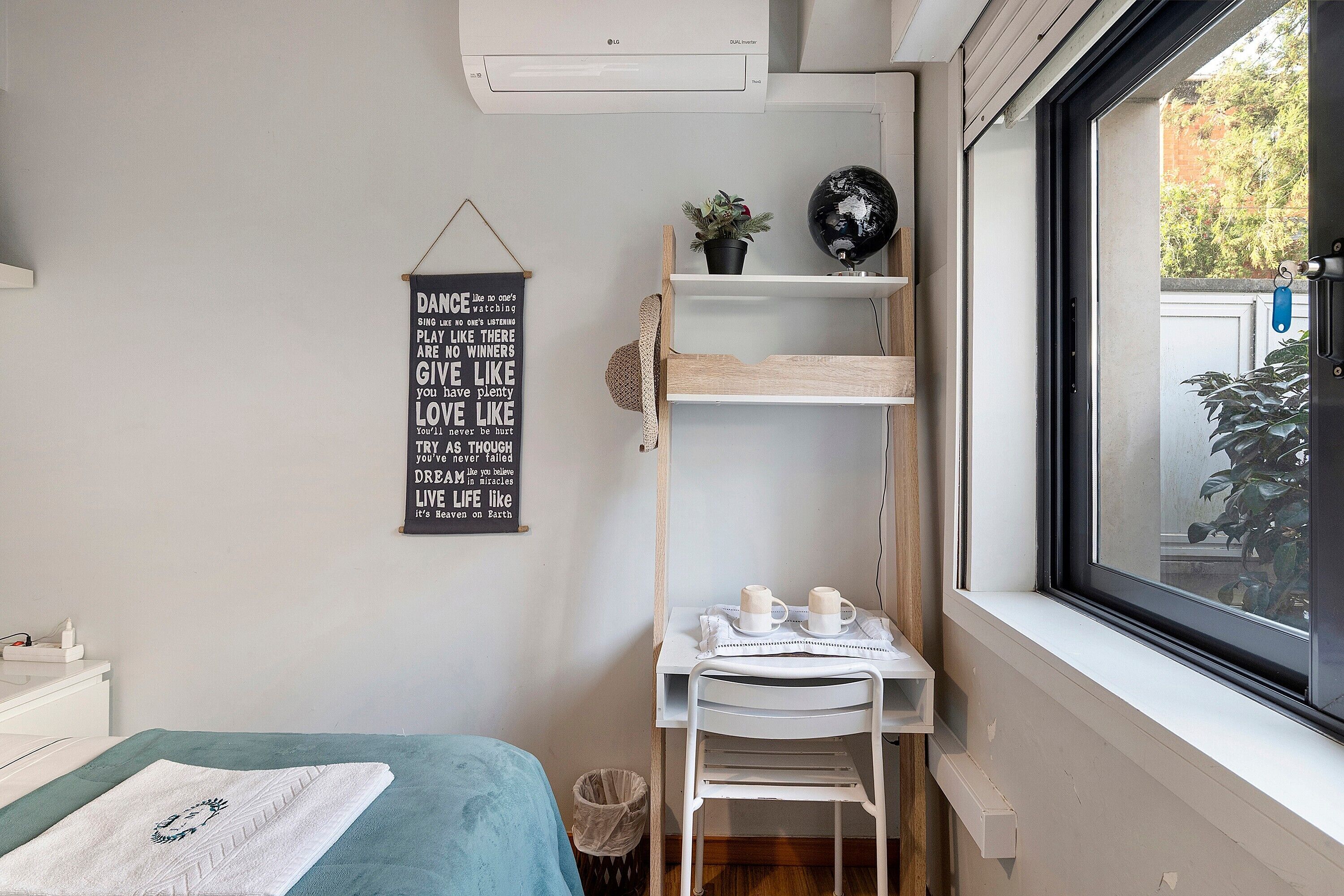 A bedroom with a bed, a desk with a chair, a window, and a motivational quote on the wall.