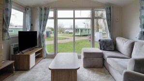 Ein Wohnzimmer mit Fernseher, einer Couch, einem Couchtisch und Blick auf ein grünes Feld sowie Wohnmobile.