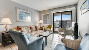 A modern living room with a sofa, armchairs, a coffee table, and a TV. - Hotel suite with beach access, shared pool - in a great location (Fort Morgan)