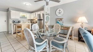 A modern kitchen with white cabinets, a glass dining table, wicker chairs, and a ceiling fan. - Hotel suite with beach access, shared pool - in a great location (Fort Morgan)