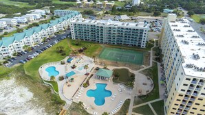 Eine Vogelperspektive eines Resorts mit mehreren Gebäuden, einem Schwimmbad, Tennisplätzen und einem Strand.