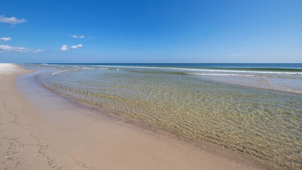 Ein Strand mit klarem Wasser, sandigem Ufer und blauem Himmel.