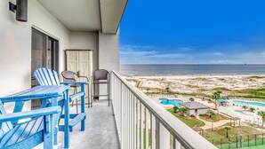 Ein Balkon mit blauen Adirondack-Stühlen, einem Tisch und Blick auf Strand und Poolbereich.